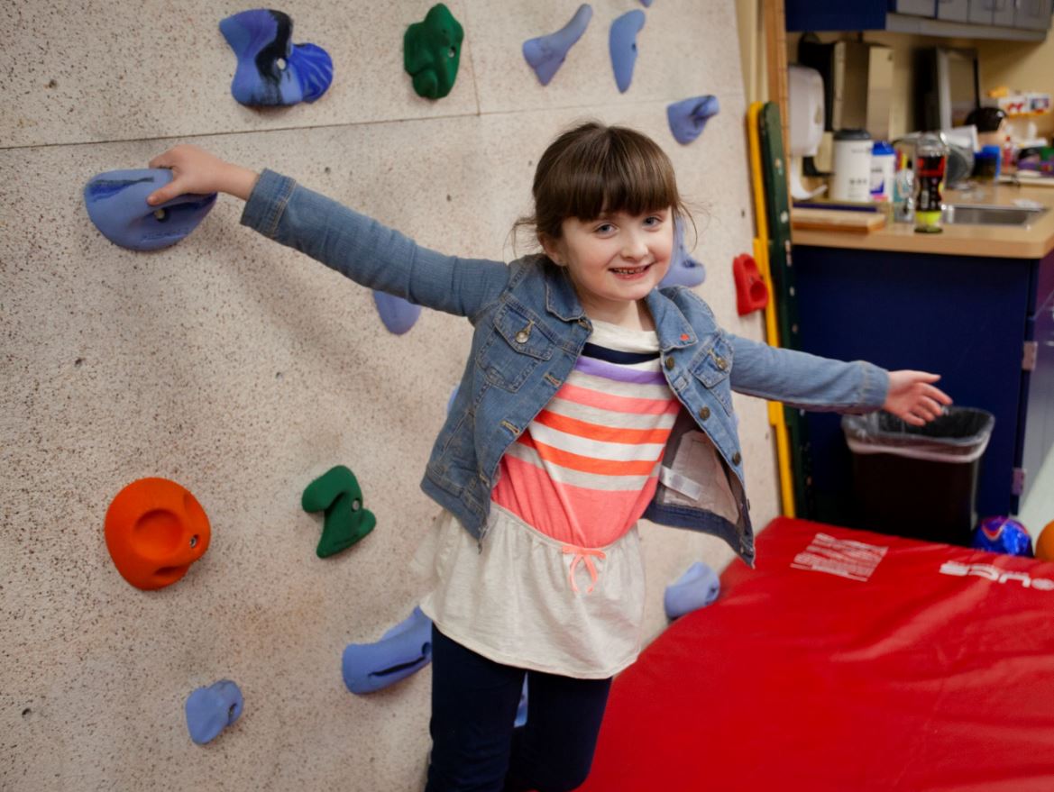 Amelia, a patient Saint Luke's The Children's SPOT, standing by the climbing wall