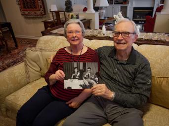 The Zollar's, Bishop Spencer Place residents, sitting on their couch, holding a black and white photo from when they were a younger couple