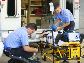 Two first responders treating a patient by an ambulance