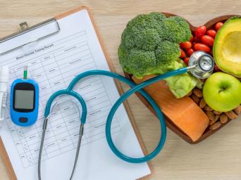blood glucose testing paper with a stethoscope and a heart shape bowl with healthy foods to fight diabetes
