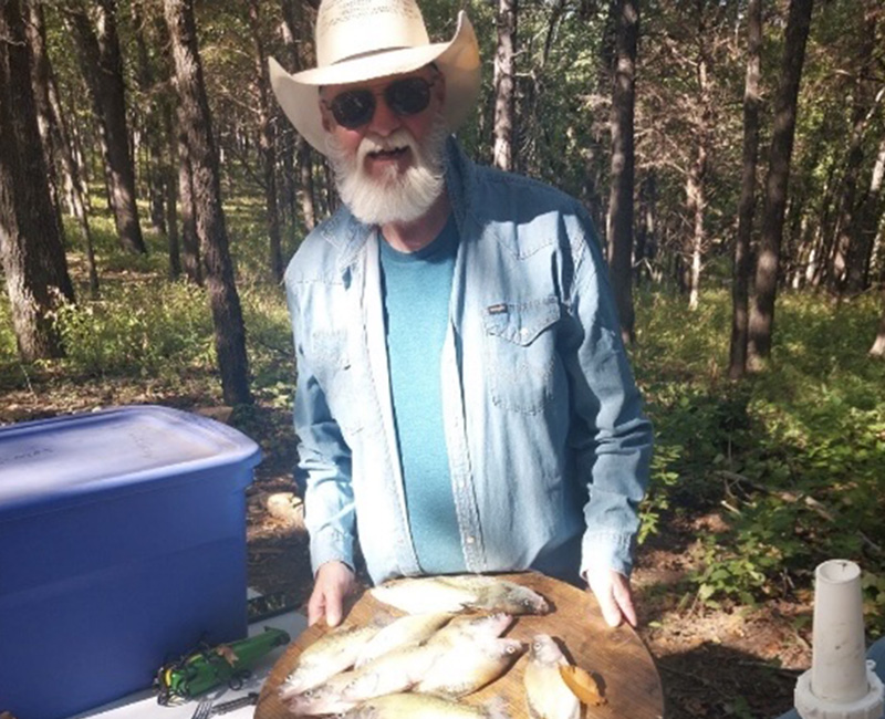 Craig Rhoads in a cowboy hat and sunglasses, standing at a white table with fish on a wooden plate.