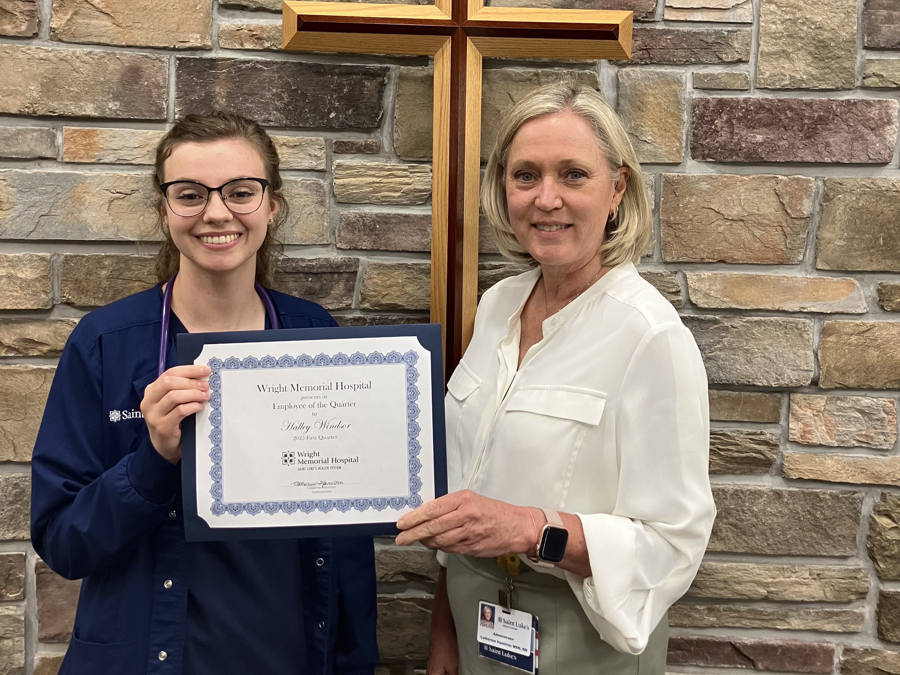Halley Windsor, handed Employee of Year Award by Catherine Hamilton (right), both standing near brick wall.