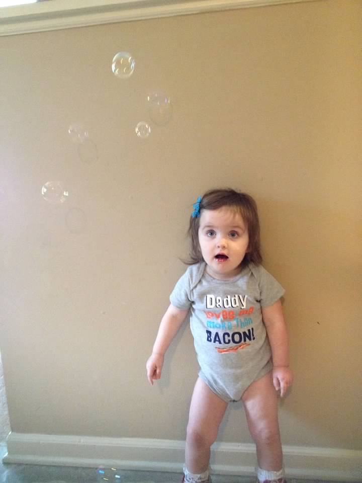 One of Amelia's first PT homework assignments was standing, leaning against a wall for support because she couldn’t stand independently. Her parents would blow bubbles and she had to reach to pop the bubbles and would stand unassisted for longer and longer. (August 2014)