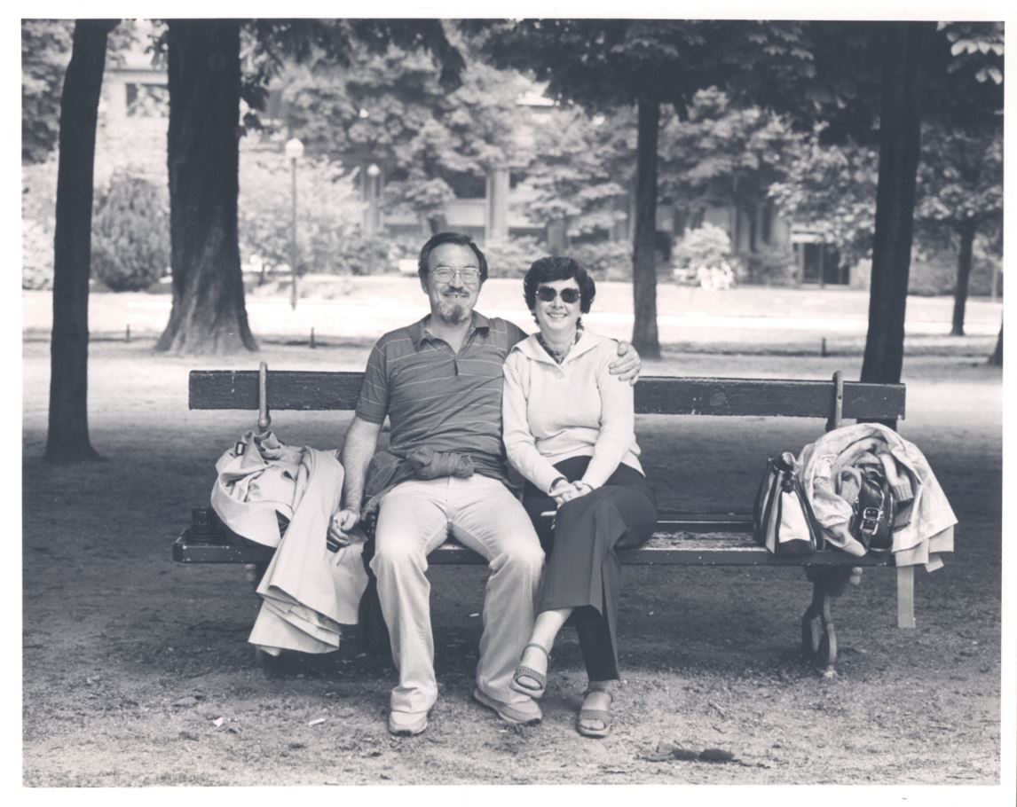 David, wrapping his arm around Joan, in a black and white photo, sitting on a park bench. 