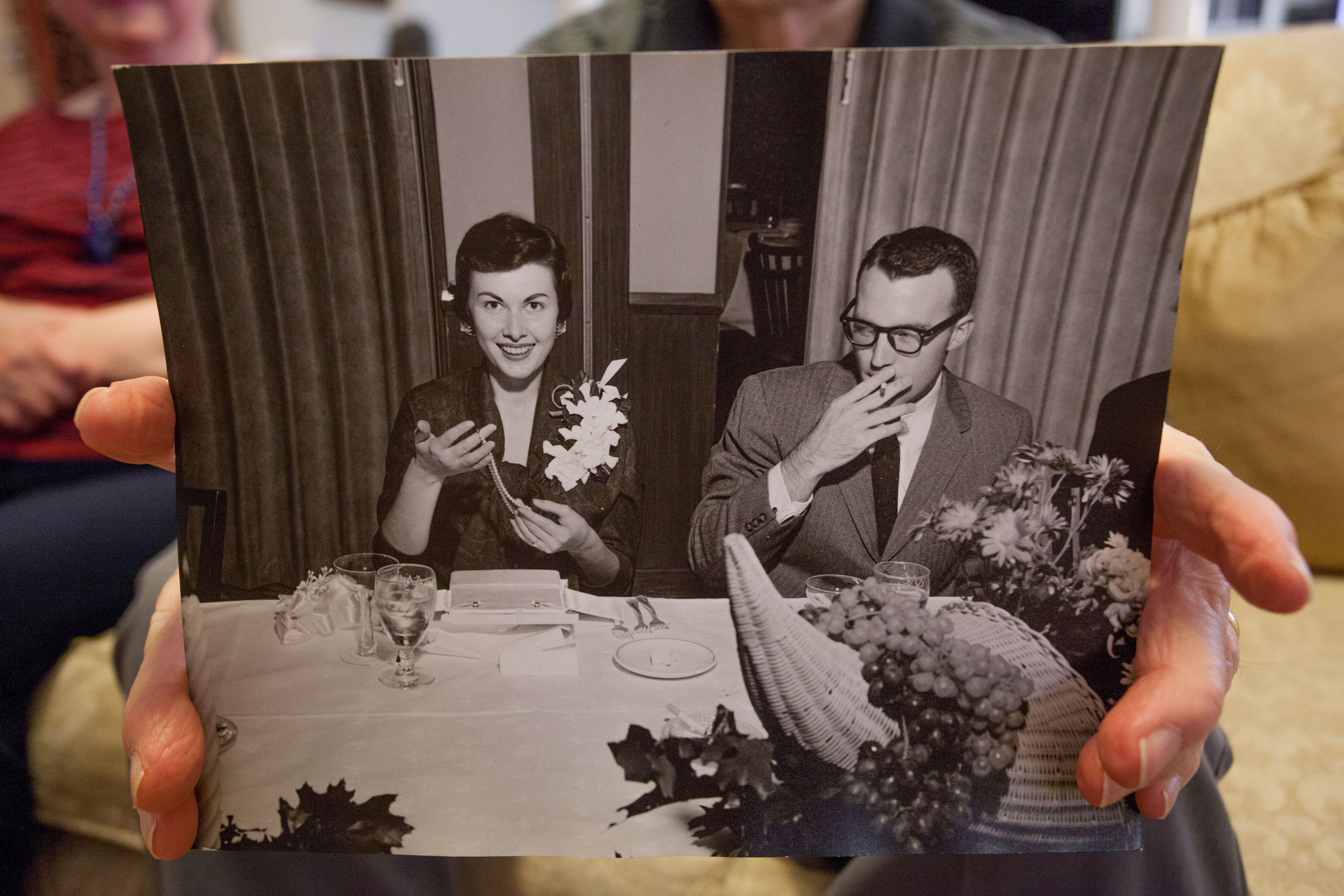 An old couples hands holding a black and white photograph of them together, smiling, as a younger couple.