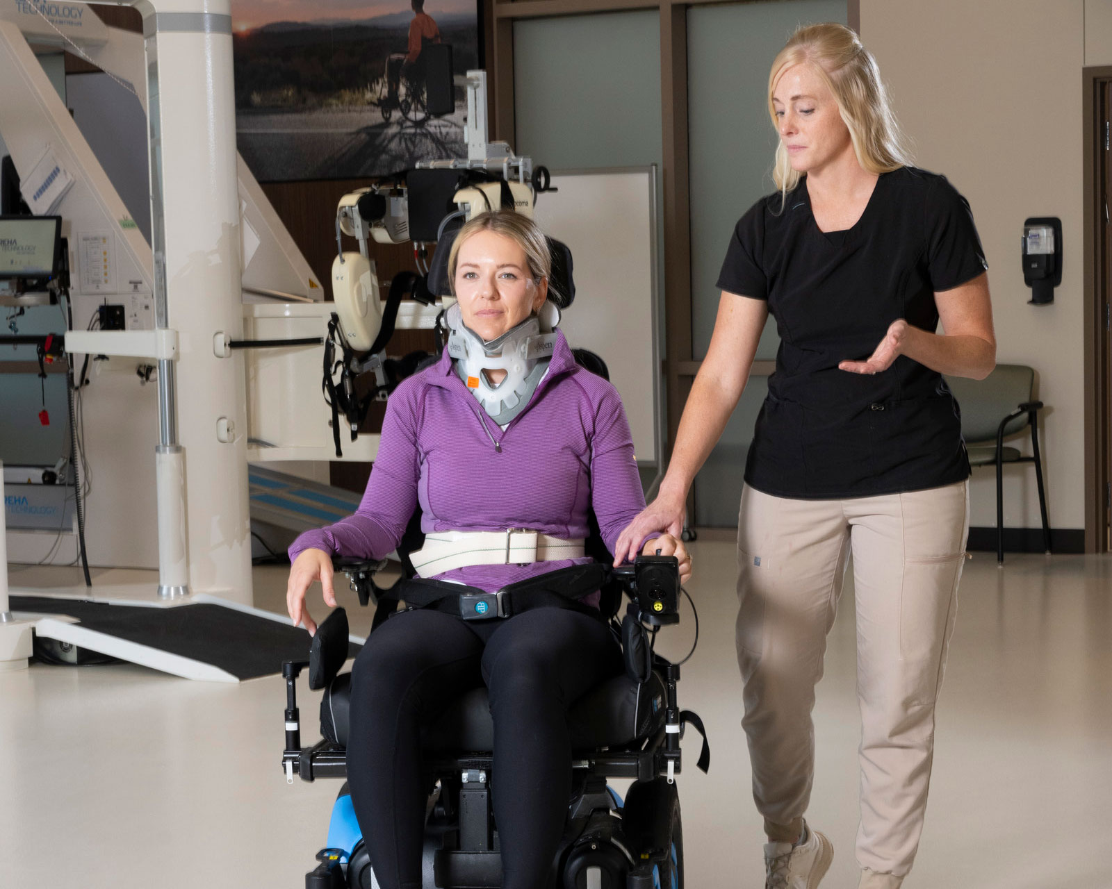 Therapist guides patient operating wheelchair in rehab gym