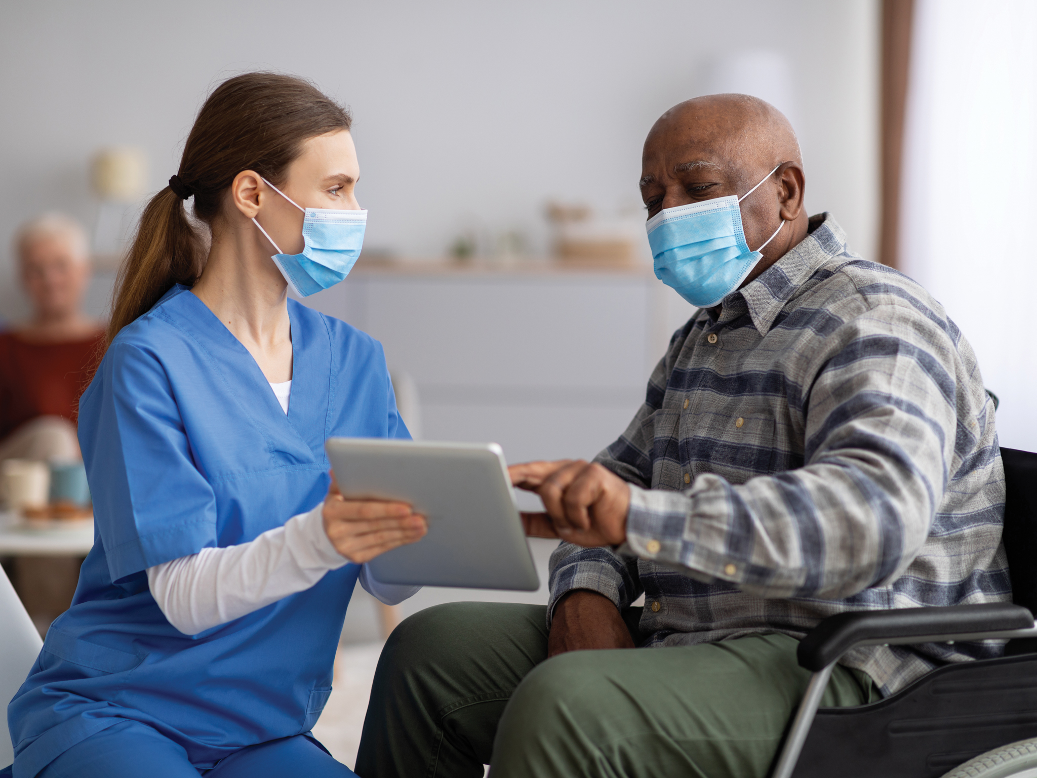 A health care provider showing a tablet to a man in a wheelchair