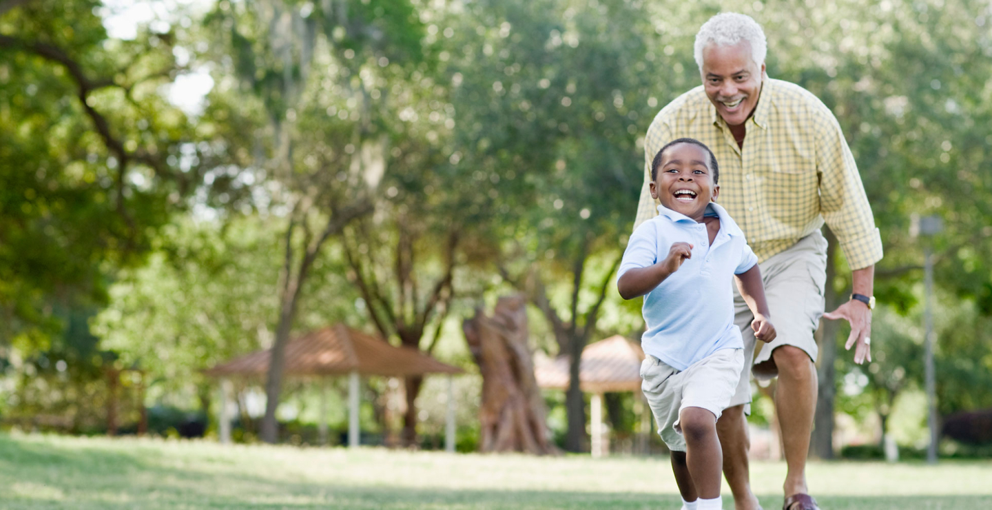 An older man is playfully chasing a child, both smiling