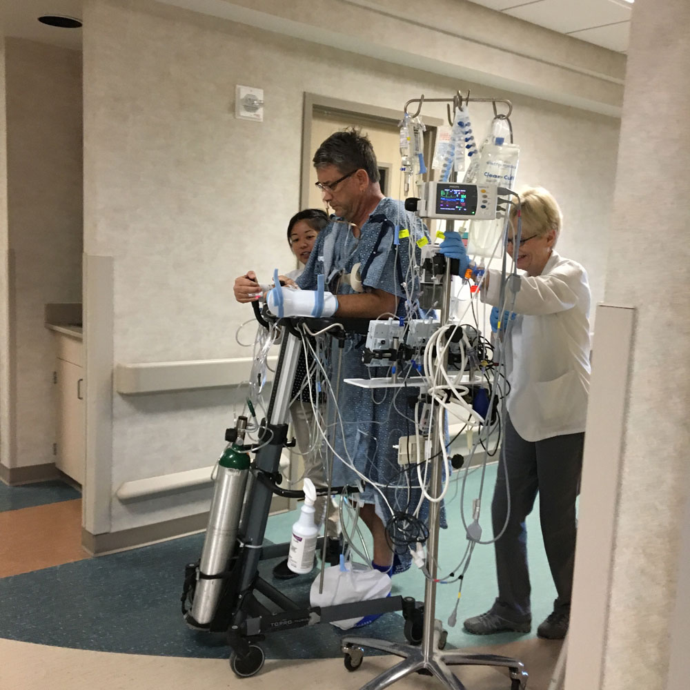 A patient is being helped down a hospital hallway with medical professionals.