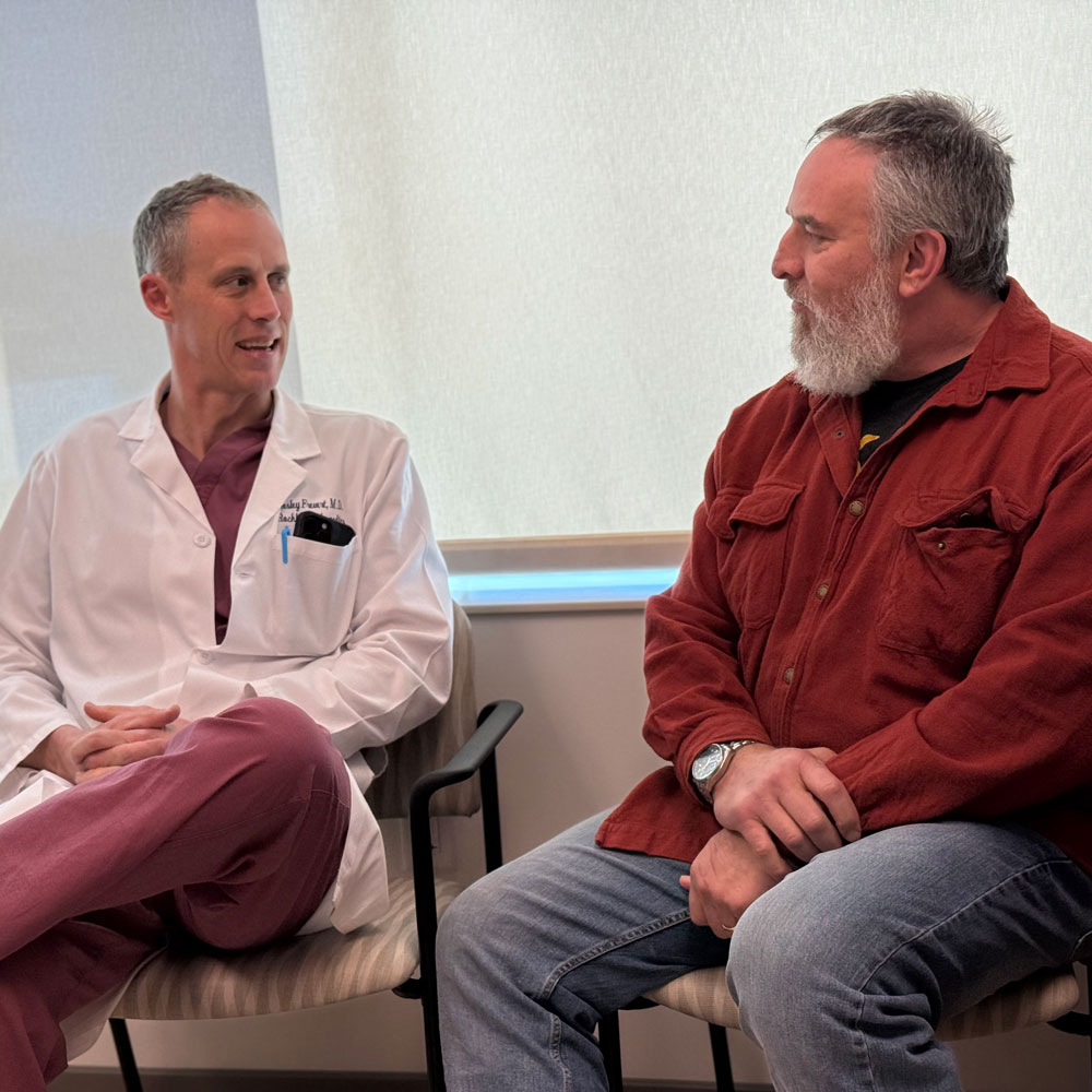 Dr. Frevert is sitting in a chair talking with Steven, a patient.
