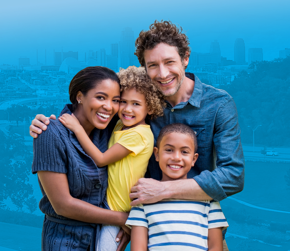 A family hugging and smiling, with Kansas City in the background.