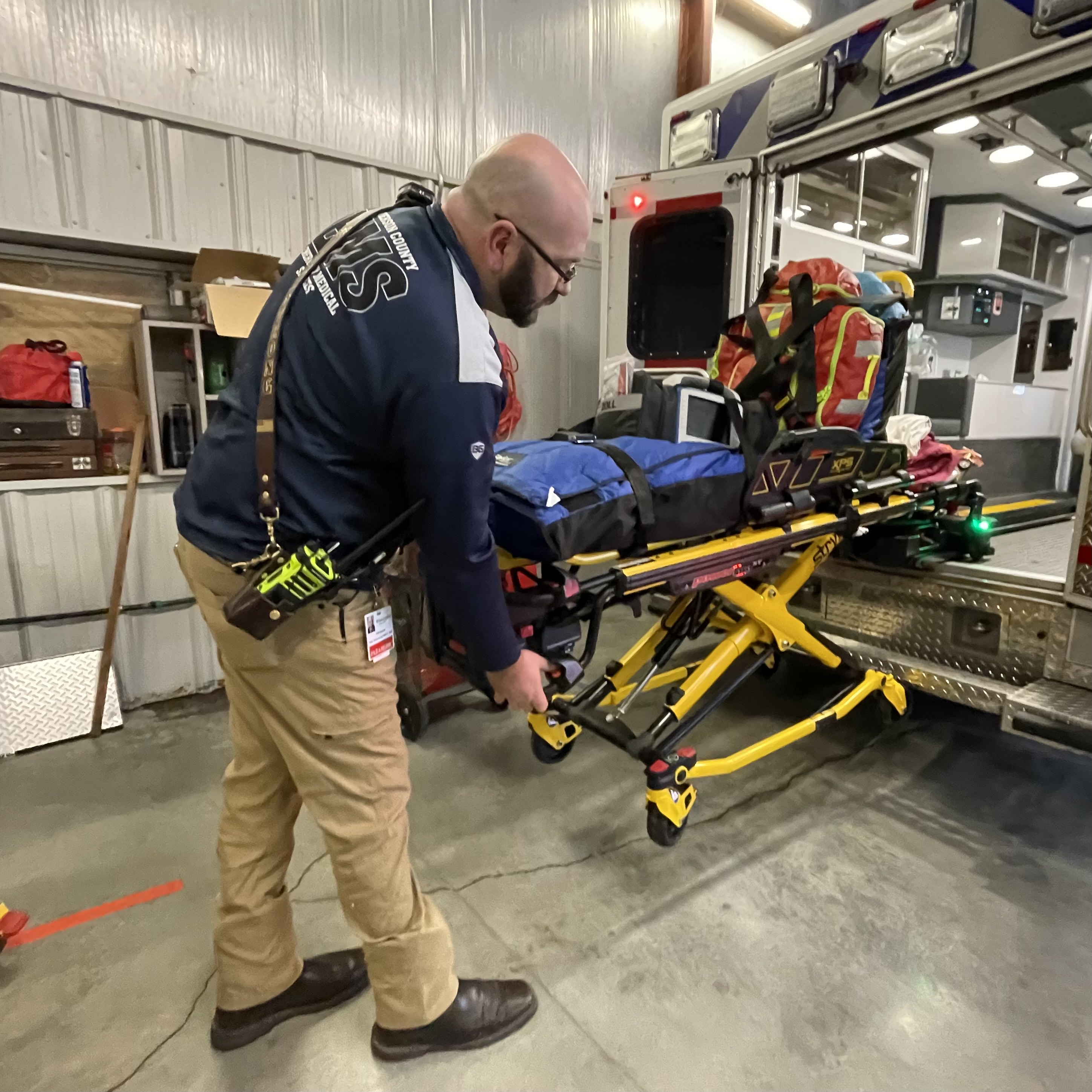 EMS team member demonstrates added safety features of stretcher outside emergency truck
