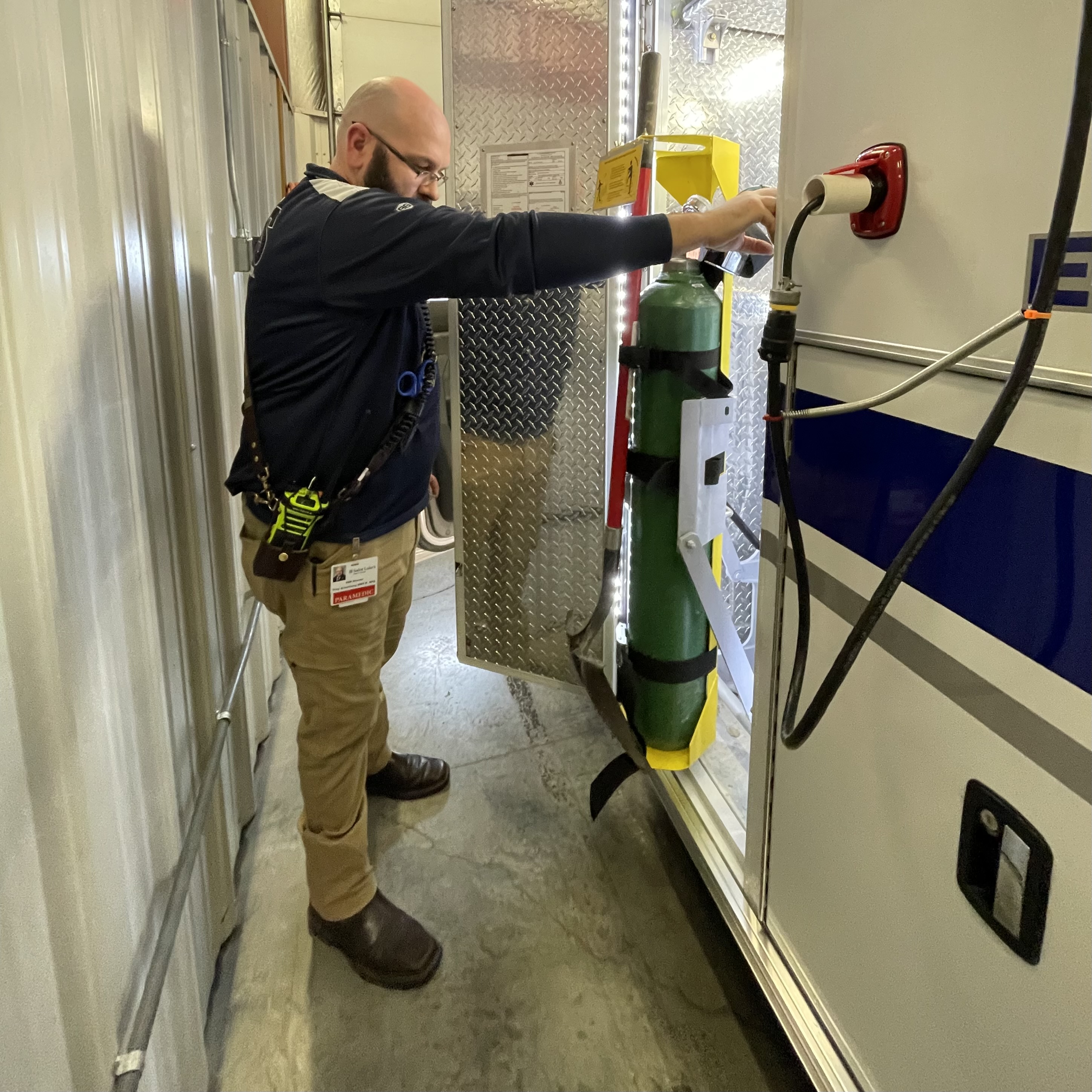 EMS team member demonstrates safety features of oxygen tank outside emergency truck