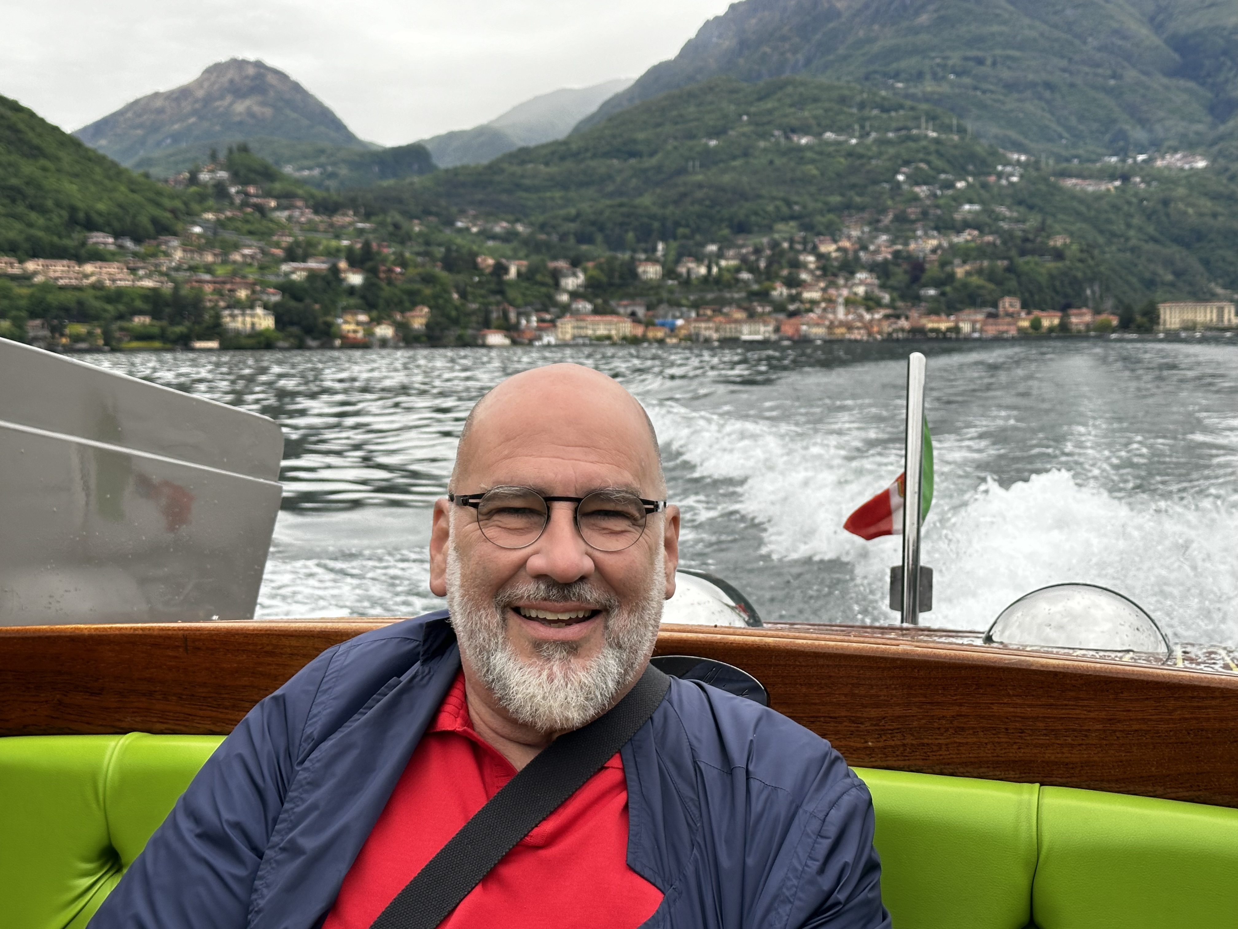 Father Greg half body shot, sitting in a canoe, overlooking mountains and homes behind him