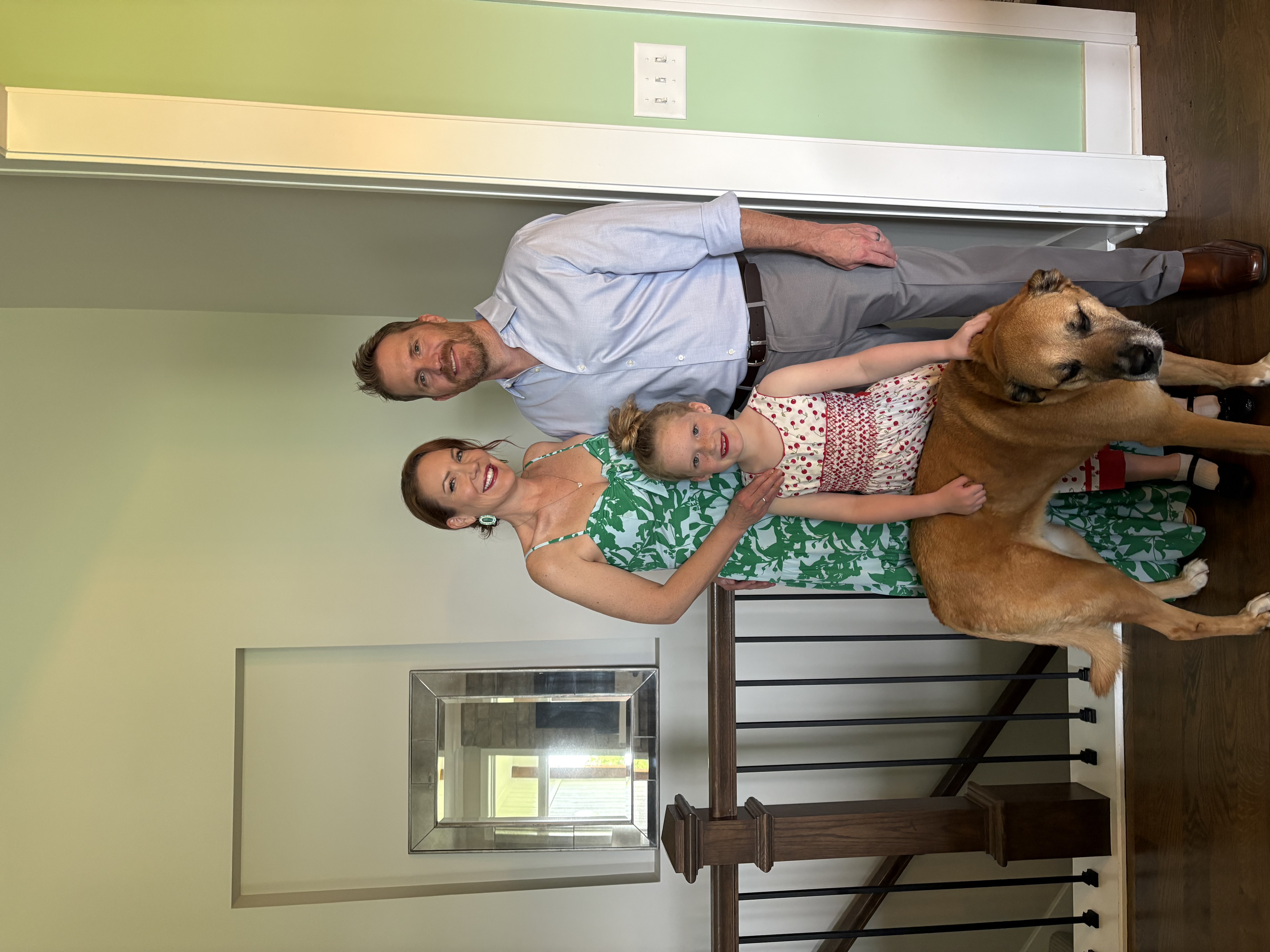 Jim (left) in a white button down and his wife in a green dress, and their daughter and dog in the middle