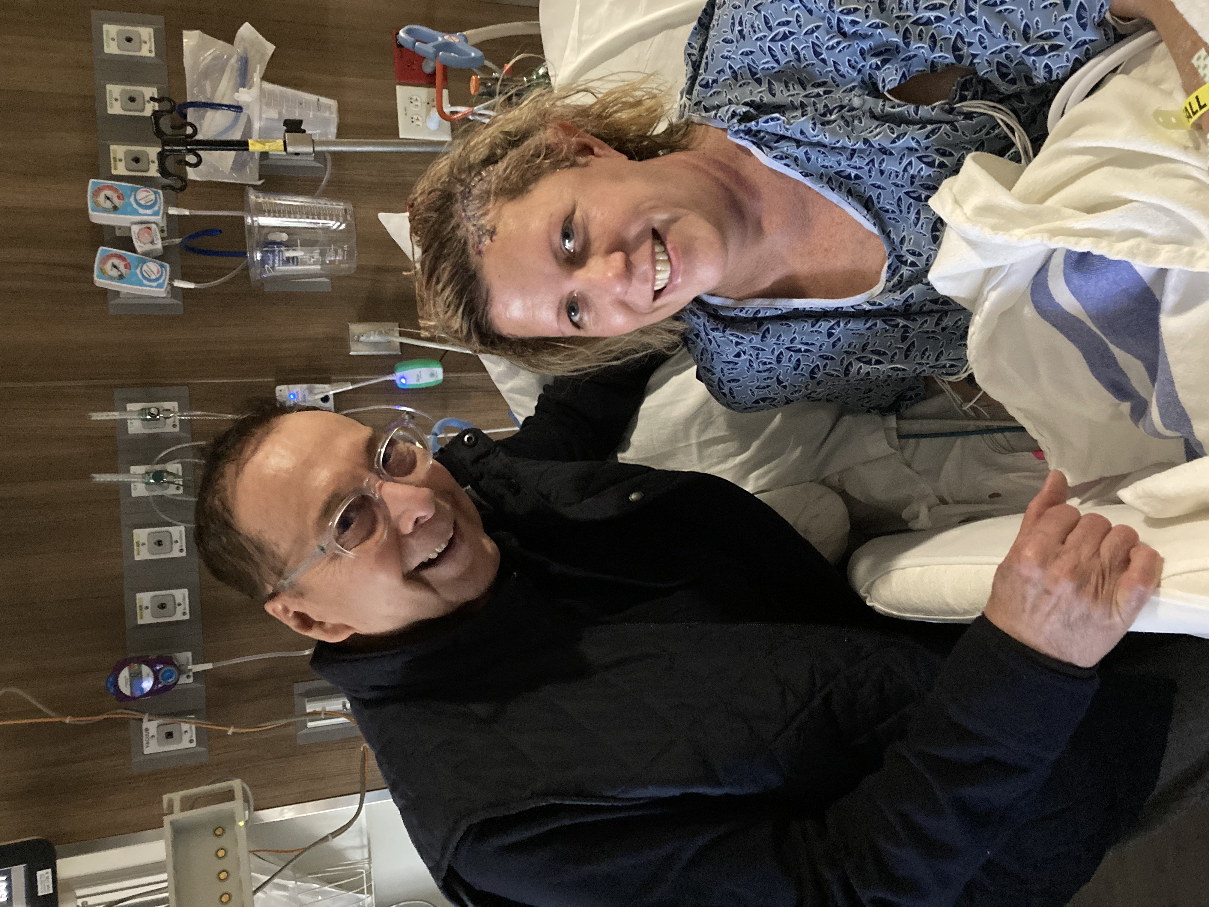 Jo Ellen Rupp, 56 on a hospital bed with her husband standing to her right side 