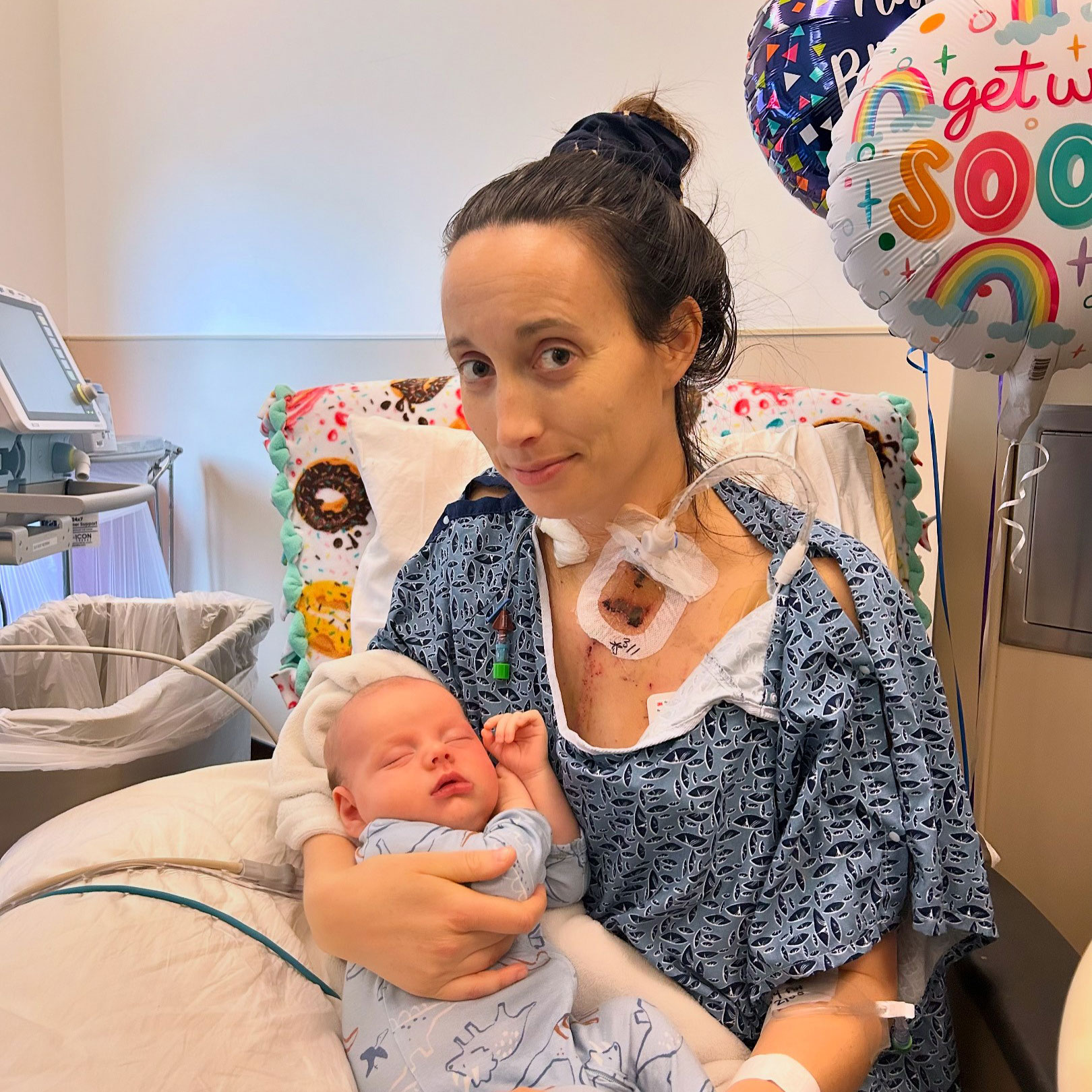 Layne is in a hospital bed hooked up with medical devices while holding a baby.