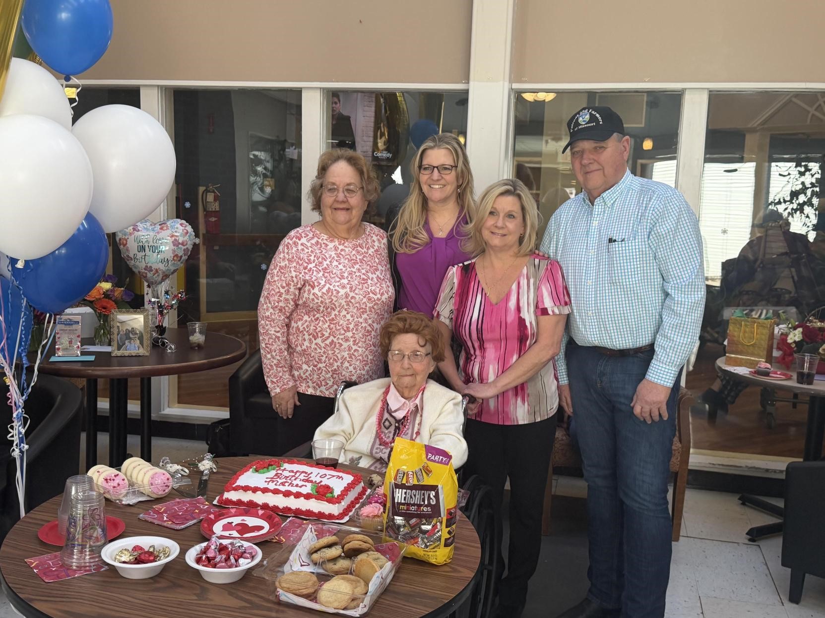 Mildred (center) seated on a brown table with cake, cookies, and candy, with four family members standing behind her.