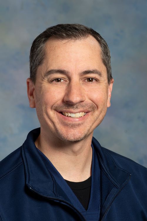 Headshot of Kirk Showalter, RN in a navy shirt with light blue background