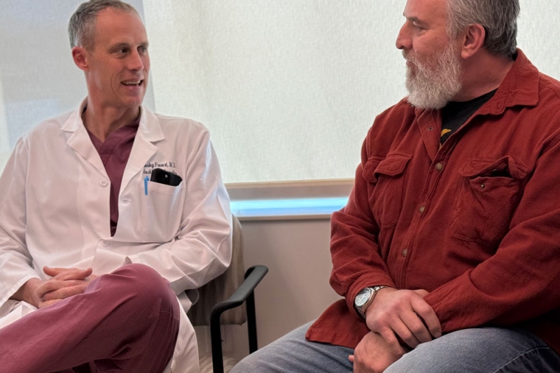 Dr. Frevert is sitting in a chair talking with Steven, a patient.
