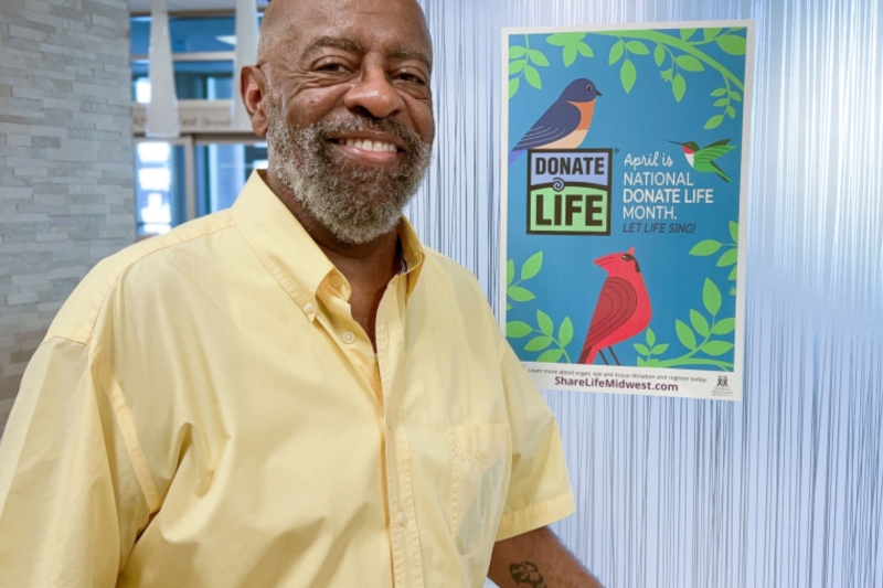 Anthony, a heart transplant patient at Saint Luke's, is smiling in front of a Donate Life poster.